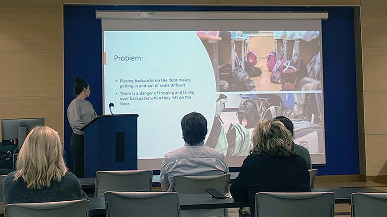 A student stands in front of a projection screen as an audience watches