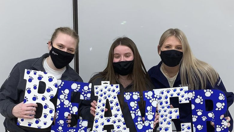 Three female students, wearing face masks, hold letters that spell Beaver