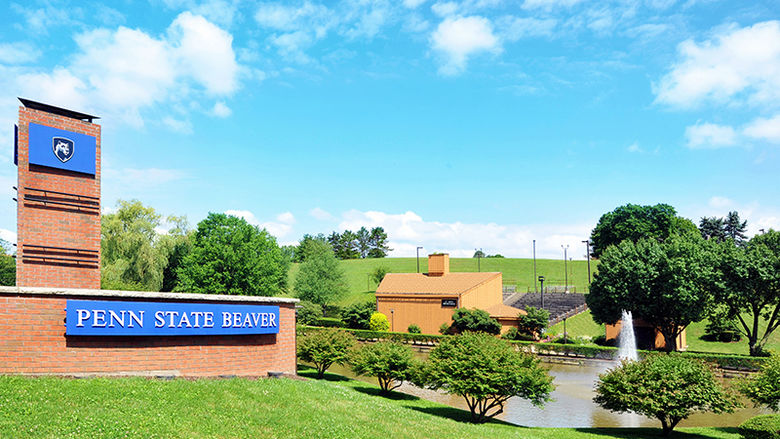 Penn State Beaver's entrance with a brick entrance wall with the campus name and the pond and amphitheater to the right. 