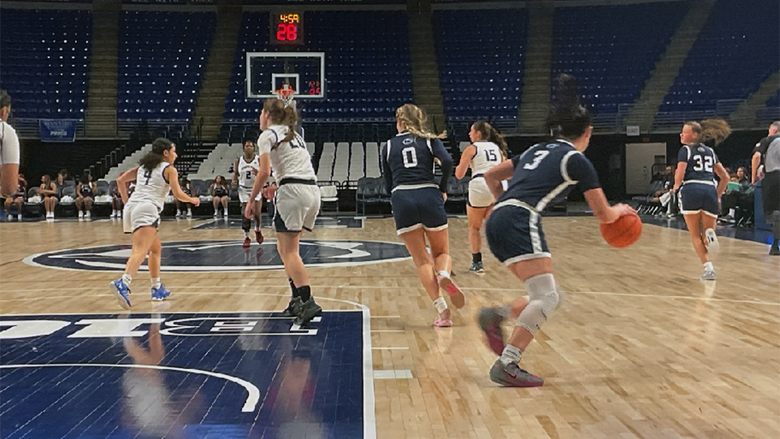 Women's basketball players wearing navy uniforms and white uniforms play on a court