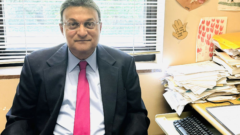 Mookerjee, wearing black suit, white shirt and red tie, sits at a desk in his office.