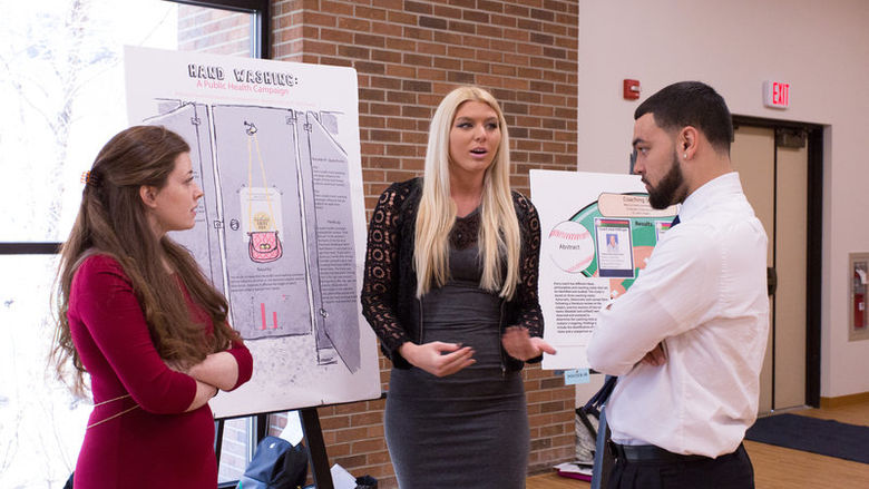 Three students gather around a posterboard to discuss their research.