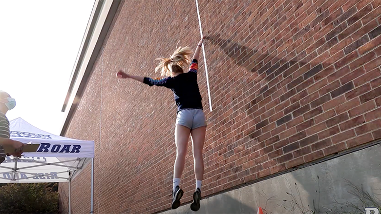 A female athlete makes a vertical jump along a brick wall to see how high she can reach.
