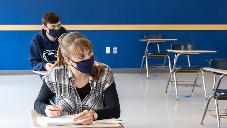 Two students wearing masks take notes in a classroom.