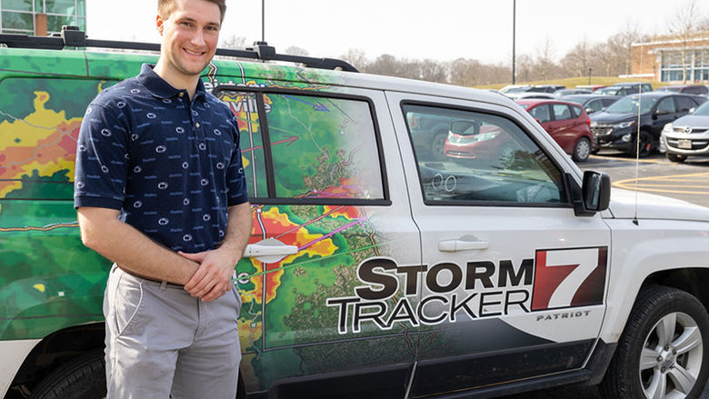Zach Petey, wearing a navy blue polo shirt and khaki pants, stands in front of the Storm Tracker 7 vehicle at Penn State Beaverthe 