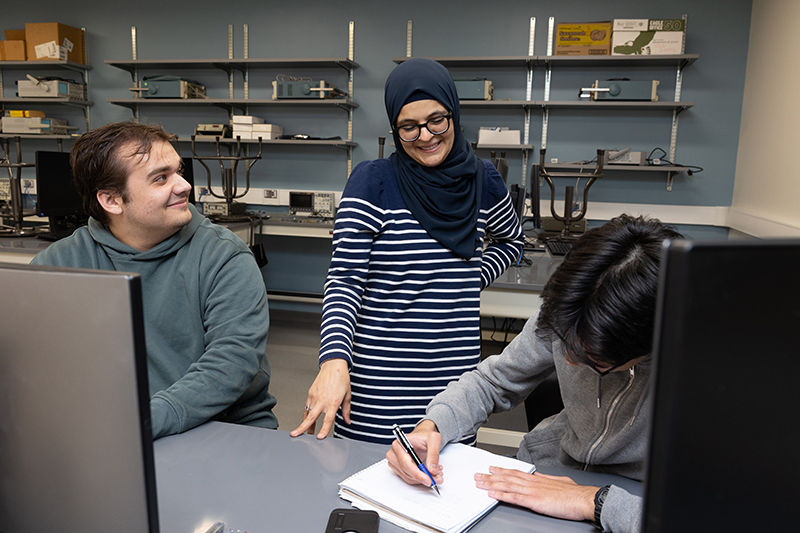 A professor works with two students in the classroom