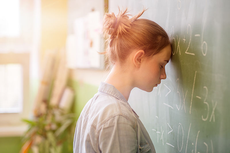 A student rests her forehead against a blackboard of math equations.