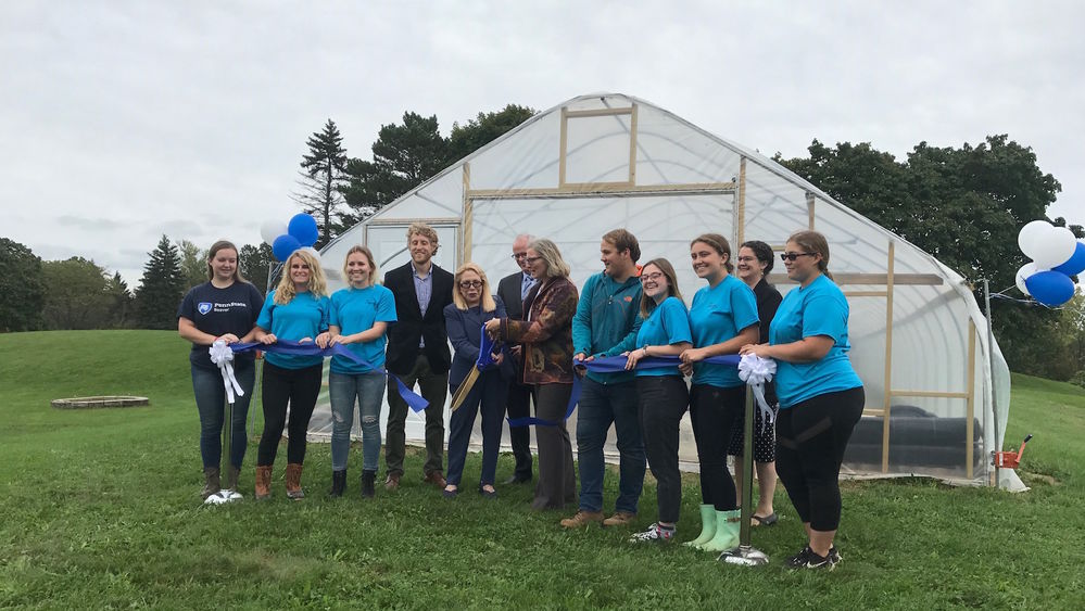 Beaver students and administators cut a ribbon in front of a high tunnel greenhouse.