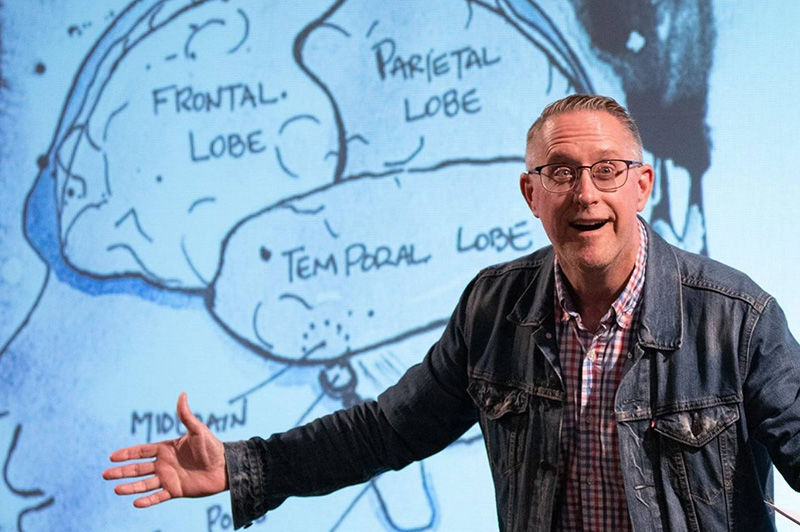 The professor gestures as he stands in front of the projected image of a hand-drawn brain.
