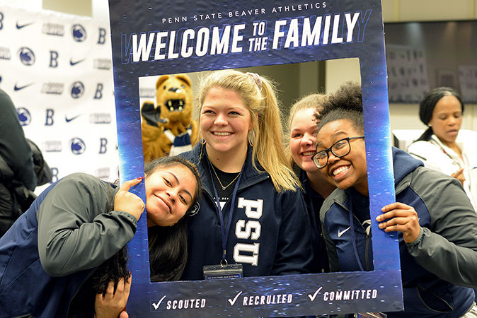 Three female students pose for a photo while holding a Penn State Welcome picture frame around themselves.