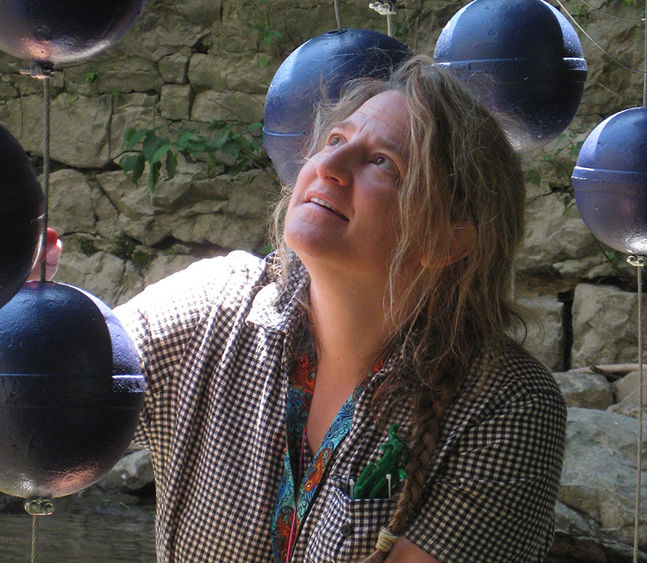 The artist is pictured standing amidst one of her creations, which is made up of suspended dark orbs.