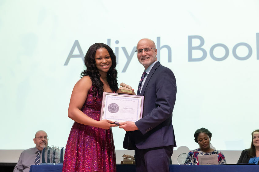 A photo of Aaliyah on stage in a fuchsia dress receiving an award from Chris Rizzo