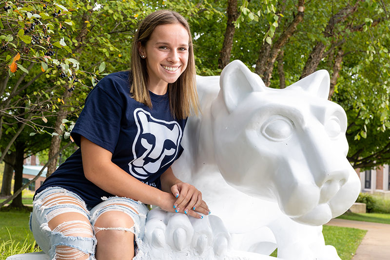 Alexis sits at the Lion Shrine on the Beaver campus wearing a navy and white Lion Ambassadors t-shirt.