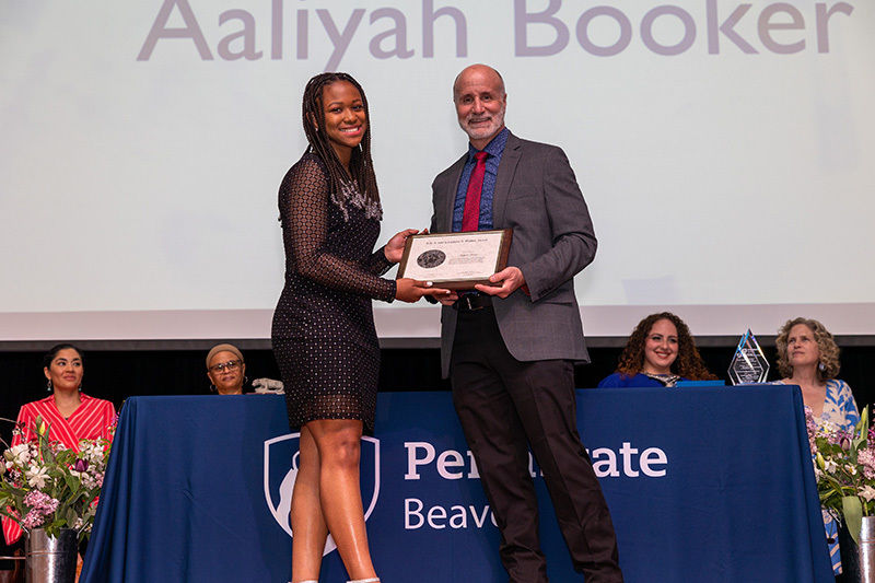 A female student is presented an award by campus staff member on stage