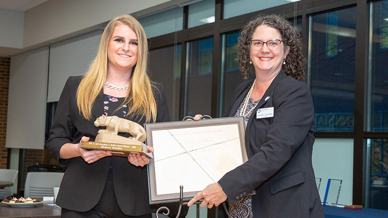 The campus chancellor stands with the award winner as they hold the plaque.