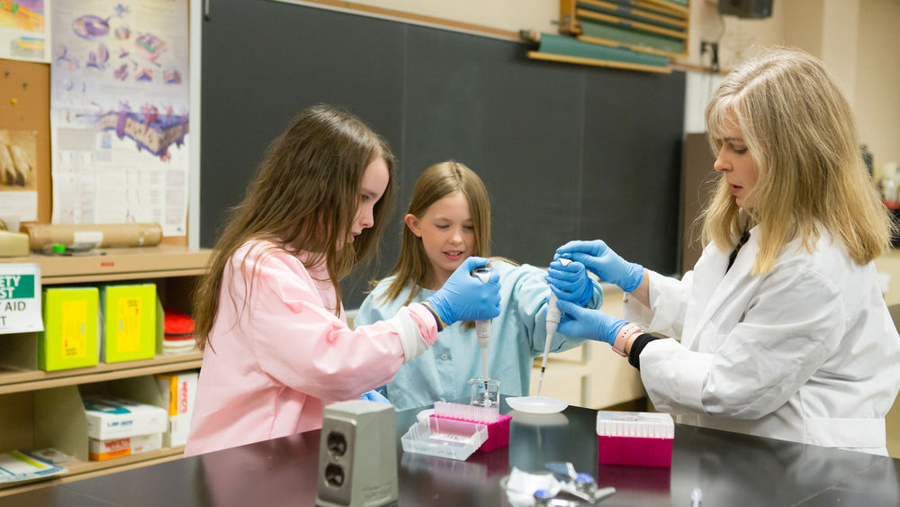 Cassandra Miller-Butterworth and two students transfer liquid into beaker.