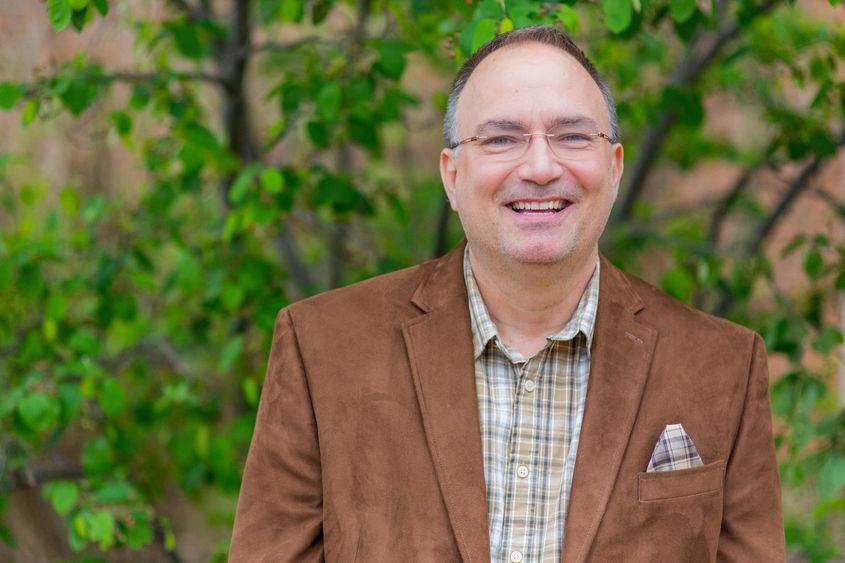 A photo of Dr. John Chapin wearing a brown blazer and standing outside