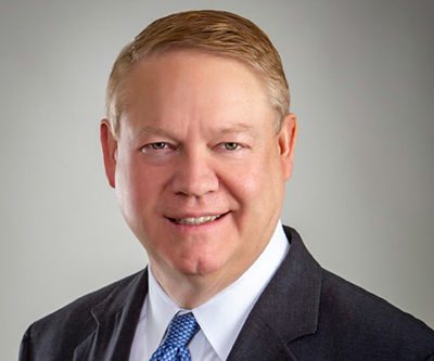 A headshot of Scott Cunningham wearing a dark suit, white shirt and blue tie.