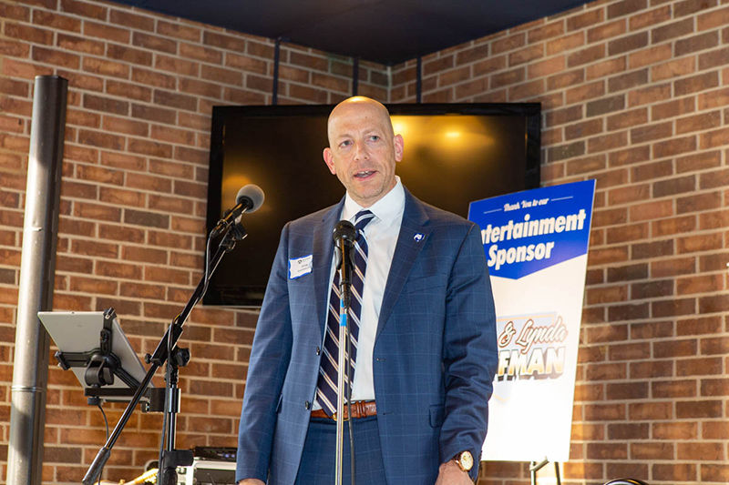 A man in a dark blue suit stands on a stage at an event