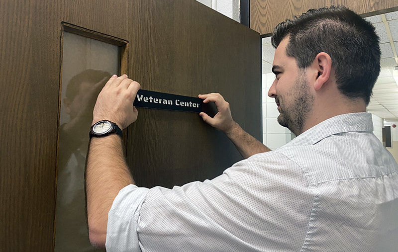 Student Josh Graham hangs a sign on the door of the new veterans lounge on campus