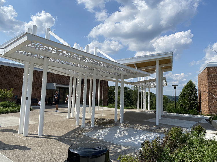 Donna Kuga Pavilion A white artistic-looking structure with a roof stands in front of a classroom building.