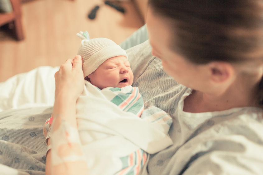 A mother holds a newborn baby swaddled in a blanket and wearing a hat