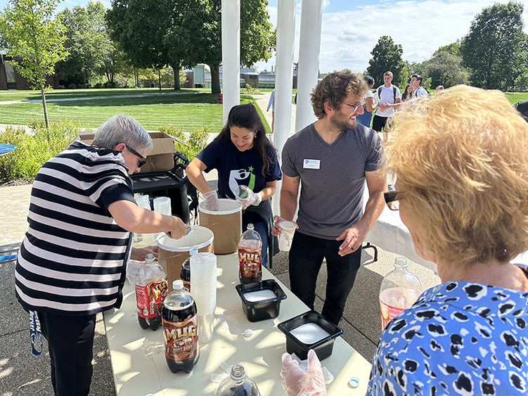 Four members of the committee stand outside on a sunny day making root beer floats.