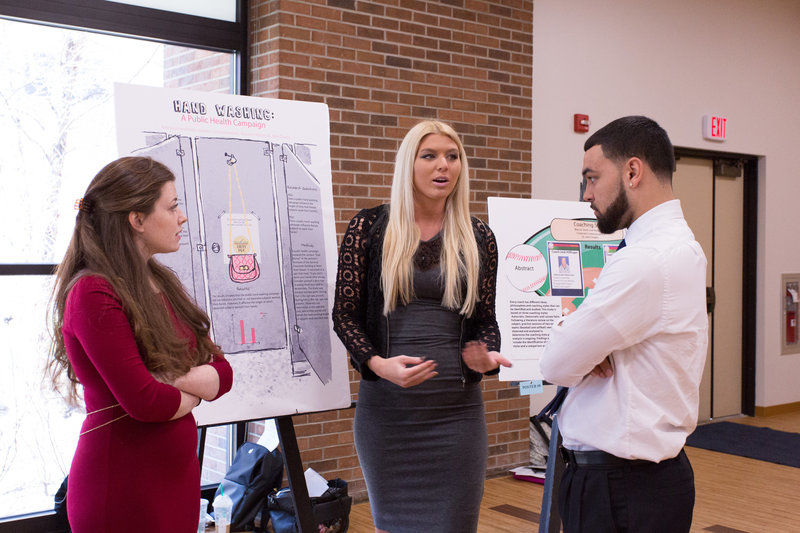 Three students gather around a posterboard to discuss their research.