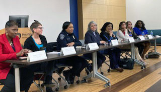 A panel of women sit behind a table in the Lodge on the campus of Penn State Beaver. There is a name card in front of each panelist.